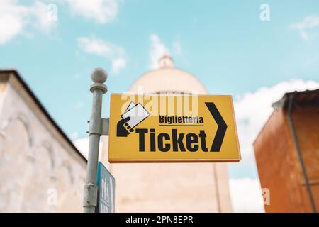 Indicatore giallo e freccia che indica i biglietti per le strade di Pisa. Cielo blu nuvoloso sopra. Foto di alta qualità Foto Stock