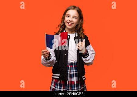 Ragazza che indossa abiti da scuola e tiene la piccola bandiera nazionale di Francia. Teen schoolgirl mostra come, pollici in su, segno di approvazione Foto Stock