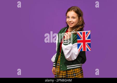 Ragazza che indossa abiti da scuola e tiene la piccola bandiera britannica. Studentessa teenager con bandiera britannica. Concetto di studio nel Regno Unito di Gran Bretagna. L Foto Stock