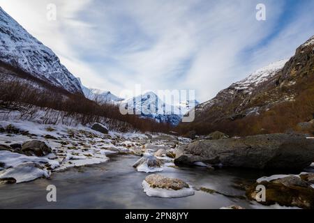 Un paesaggio panoramico di un fiume che scorre attraverso una catena montuosa innevata, circondata da grandi rocce e massi Foto Stock