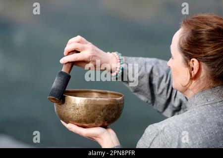 La ciotola tibetana viene utilizzata nella terapia del suono, nella meditazione e nello yoga. Donna che pratica una ciotola di canto per la terapia del suono in atmosfera per la guarigione, meditazione e Foto Stock