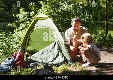 Ritratto dell'uomo adulto come capo scout che insegna al bambino come impostare le tende nella foresta Foto Stock