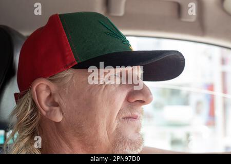 uomo maturo in un berretto alla guida di un'auto. guida e trasporto di passeggeri. Foto Stock