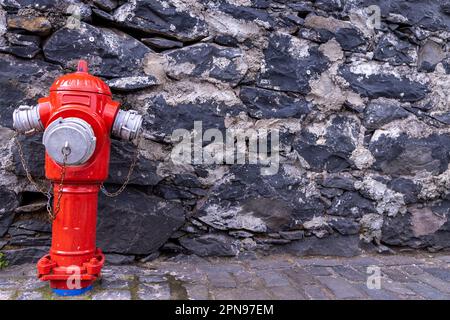 Un tubo rosso idrante usato da combattimenti antincendio per attaccare ai loro motori antincendio per pompare acqua per spegnere incendi su un muro di mattoni situato nella città di Fun Foto Stock