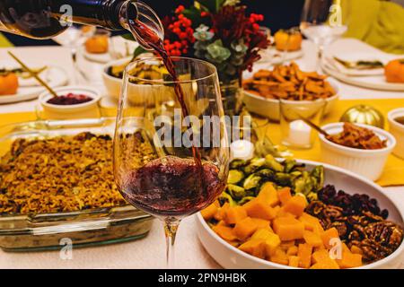 Vino rosso versato in un bicchiere in piedi sul tavolo della cena del Ringraziamento, primo piano Foto Stock