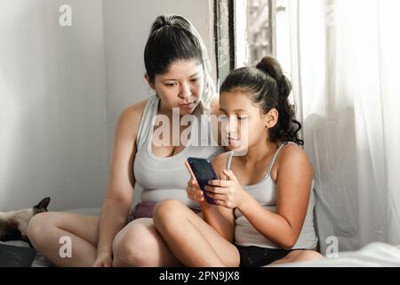 giovane madre che guarda curiosamente ciò che sua figlia sta facendo sul suo telefono cellulare Foto Stock