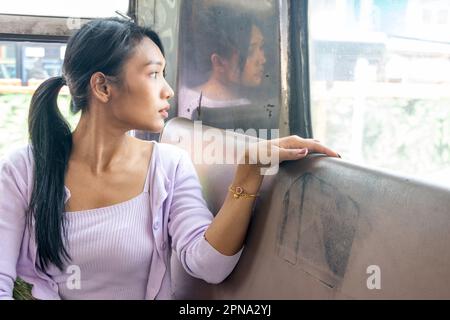 Una giovane donna siede su un vecchio autobus e guarda indietro attraverso il finestrino posteriore Foto Stock