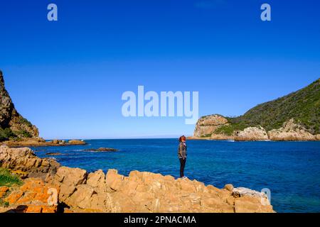 Uomo in piedi su rocce di fronte a Knysna Heads, ingresso laguna, costa rocciosa, Knysna, Garden Route, Capo Occidentale, Sudafrica Foto Stock
