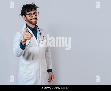 Sorridente medico che indica voi isolato. Giovane medico che ti indica. Medico amichevole che indica la macchina fotografica Foto Stock