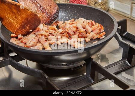 La pancetta tritata con le cipolle viene fritta in padella su stufa a gas Foto Stock