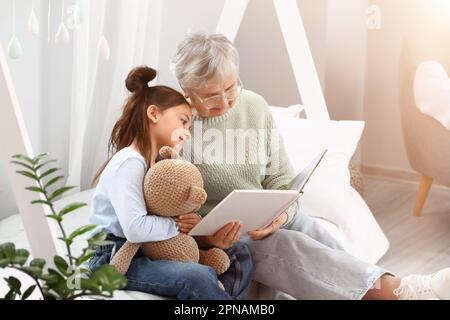 Bambina con giocattolo e sua nonna che legge il libro in camera da letto Foto Stock
