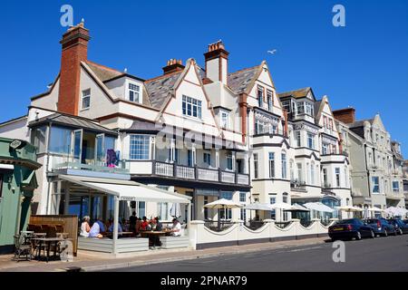 I turisti si rilassano in una caffetteria sul marciapiede accanto agli hotel sul lungomare, Sidmouth, Devon, Regno Unito, Europa. Foto Stock