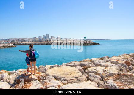 Madre e figlio guardano il porto sul faro che segna la fine dei moli rocciosi Farol de Quarteira in albufeira algarve portogallo Foto Stock