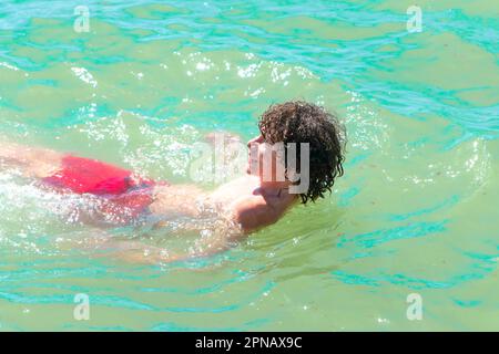 ragazzo adolescente in pantaloncini nuotando sulla schiena dopo aver saltato in mare a albufeira algarve portogallo Foto Stock