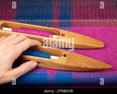 La mano prende una navetta in legno con filo blu per fare un progetto di tessitura, fuoco selettivo. Lavoro di primo apparire di mano Foto Stock