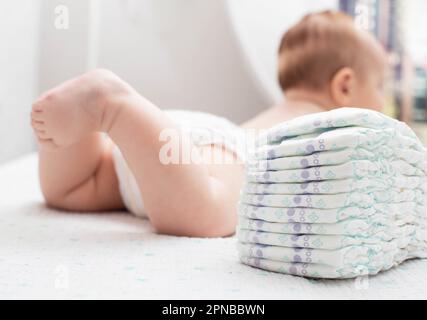 Le gambe di un bambino in un pannolino sullo sfondo di una pila di pannolino confortevole per bambini. Foto Stock