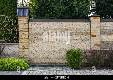 Moderna struttura in mattoni con recinzione in pietra chiara e pali di fronte ad un edificio residenziale. Foto Stock