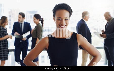 Un atteggiamento positivo è sempre la chiave. una donna d'affari attraente sorridente alla macchina fotografica mentre i colleghi sono sfocati in background. Foto Stock