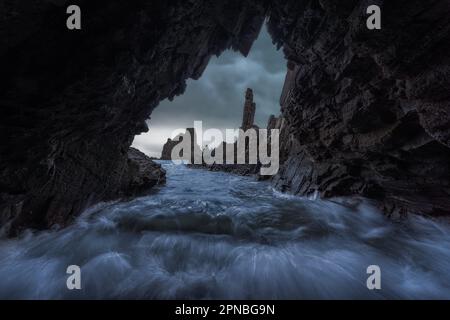 Lunga esposizione di Arrecife de las Sirenas Cabo de Gata formazioni coralline Almeria da una grotta scura con onde di mare schiumose sotto il cielo nuvoloso di giorno Foto Stock