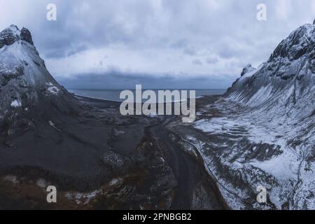 Veduta aerea dell'acqua di mare circondata da montagne innevate sotto il cielo nuvoloso il giorno d'inverno in Islanda Foto Stock