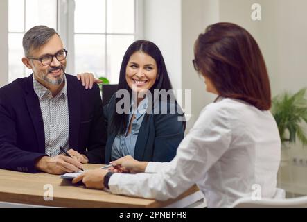 Ritratto di un uomo attraente e felice e di due belle, giovani donne che parlano in un ambiente di lavoro, seduto su una scrivania in ufficio. Foto Stock