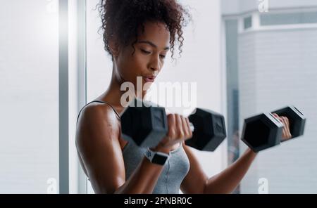 Mostra i tuoi muscoli che boss. una giovane donna che si allenava con i manubri in palestra. Foto Stock