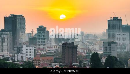 Il sole dorato pende basso sopra la capitale della Cambogia, è zona affollata di Riverside sulle banks.Tall edifici moderni e blocchi di appartamenti incombono Foto Stock