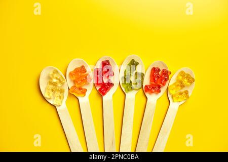 Composizione di posa piatta con deliziosi orsacchiotti di gelatina caramella in cucchiaio di legno, orsacchiotto di gommosa su sfondo giallo, vista dall'alto, spazio copia. Foto Stock