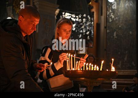 LEOPOLI, UCRAINA - 15 APRILE 2023 - Un uomo e una donna illuminano le candele durante la benedizione dei cesti pasquali nella chiesa dei Santi Pietro e Paolo Garrison su Hol Foto Stock
