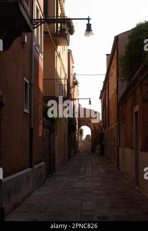 Vista dell'arco su una piccola strada con lampade da strada alla luce del sole Foto Stock