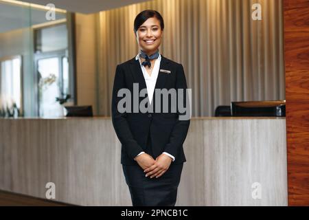 Giovane addetta al ricevimento asiatica che si sente fiduciosa nel suo abbigliamento formale, sorridendo e guardando la macchina fotografica. Dipendente dell'ospitalità femminile che lavora come concierge Foto Stock