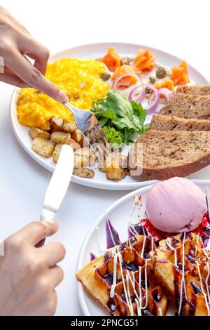 Mangiare con forchetta e coltello salmone affumicato con capperi crema aneto e uova strapazzate con pane di segale, verdure e waffle. Foto Stock