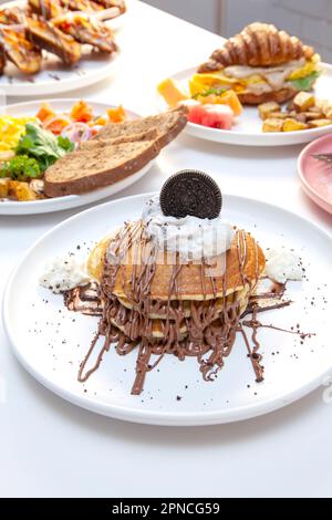 Gocce di cioccolato su torta tagliata in padella con altri piatti per la colazione sullo sfondo. Foto Stock