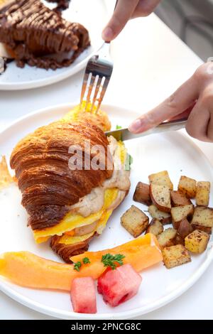 Colazione a sandwich con uova e croissant con cocomero fresco, frutta e patate. Foto Stock