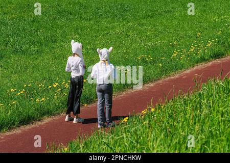 Primavera, estate, prato fiorito, vista posteriore delle ragazze in costume coniglietto che camminano io e giocare nel parco Foto Stock