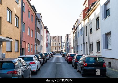 Corsia cittadina stretta con auto parcheggiate strettamente su entrambi i lati. Cielo sbiadito e incolore sopra gli edifici residenziali. Foto Stock