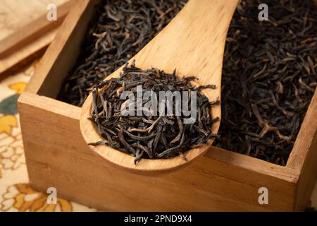 Assam indiano nero Harmutty foglie di tè secco su un cucchiaio di legno in una scatola da tè primo piano Foto Stock