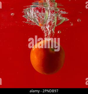 Pomodoro maturo cade profondamente sotto l'acqua con un grande splash. Foto Stock