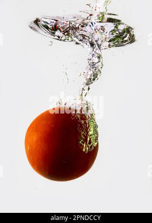 Pomodoro maturo cade profondamente sotto l'acqua con un grande splash. Foto Stock