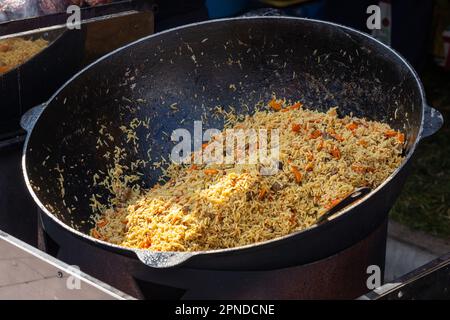 Pilaf caldo in grande calderone all'aperto. Cibo orientale tradizionale. Concetto di Street food. Primo piano Foto Stock