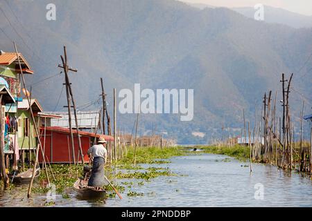 Un uomo rema su una tradizionale barca di legno nelle acque del Lago Inle, Stato di Shan, Myanmar. Foto Stock