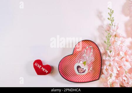 Ogni giorno è il giorno della mamma. I concetti del giorno della madre e del giorno più bello, concetto dell'amore. Cuore rosso con la lettera AMORE MAMMA con bel fiore su sfondo rosa Foto Stock