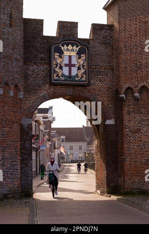 Una giovane donna sta guidando con gioia una bicicletta attraverso un arco in un paesaggio urbano Foto Stock