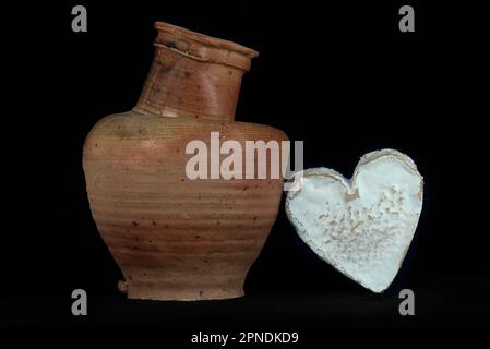 Vita morta con un formaggio Neufchatel Normand (A.O.P.) e una brocca di terracotta, su sfondo nero Foto Stock