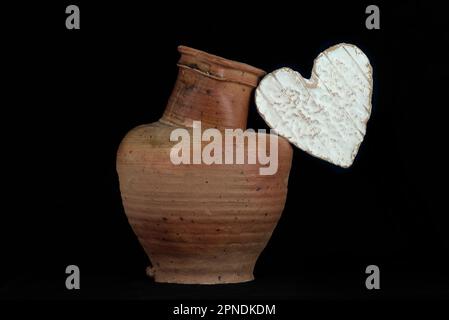 Vita morta con un formaggio Neufchatel Normand (A.O.P.) e una brocca di terracotta, su sfondo nero Foto Stock