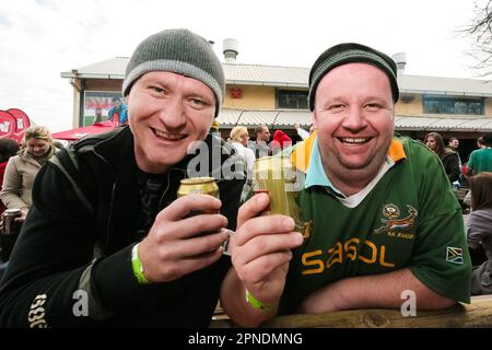 Un primo piano di due amici maschi felici che si posano sorseggiando una birra insieme Foto Stock