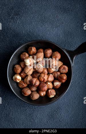 Nocciole crude in una ciotola su fondo nero. Noci in una ciotola su uno sfondo scuro. Foto Stock