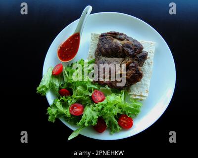 Piatto bianco con carne croccante, verdure, pane sottile e salsa sulla superficie nera Foto Stock