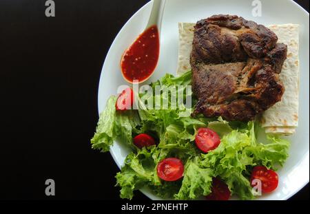 Concetto per il menu del ristorante o carta da parati con carne fritta, verdi e salsa rossa su un piatto bianco in un lato dell'immagine Foto Stock