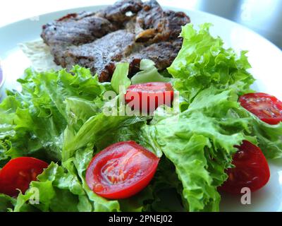 Servire per carne a metà pomodoro fresco su foglie di lattuga cosparse di olio d'oliva Foto Stock